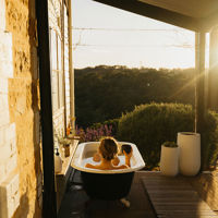 A woman sits in the outdoor bathtub on the verandah next to the cottage which has views out to the garden
