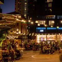 People sit at tables under fairy lights scattered around Festival Plaza