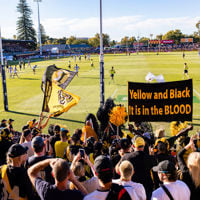 Sign and flags fly high in the stands which cheer on the players on the football field during AFL Gather Round