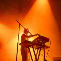 Silhouetted musician plays on stage during Illuminate Adelaide surrounded by an orange glow