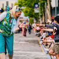A float member smiles brightly as she goes to high five a child's hand clapper. 