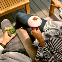 Two people enjoying cocktails outdoors at Sunny Hill Distillery — a pink gin drink and a mojito.