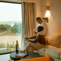 A couple hold glasses of red wine while sitting on the couch looking out the window at Rumi on Louth