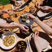 Girl feeds her friend across the table outside among the gardens at Coriole