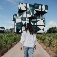 Woman walking towards a giant Rubik's cube like building called d'Arenberg, with green vines either side