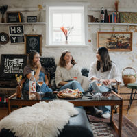 Three woman sitting on a leather couch inside Hither & Yon, with old knickknacks and paintings around them