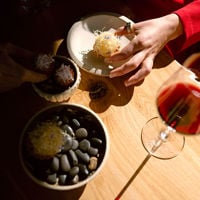 Close up of a small morsel of food plated artfully on rocks with a red wine in view