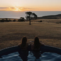 Two friends watch the sunset over the paddocks and ocean from the end of the hot tub at Saltbush Farm. 