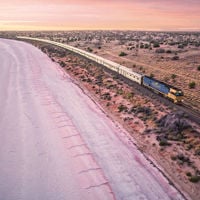 A bird's-eye view of The Ghan train going past a fairy floss pink Lake Hart