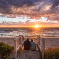A couple sitting on wooden stairs looking out at the sunset over Henley Beach 