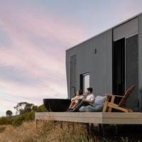 A couple sit on the deck of their luxurious black cabin toward the view 