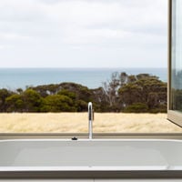 An indoor bath with an open window overlooks shrubbery and ocean views