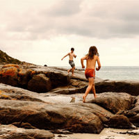 Two kids walking on a rocky coastal landscape nearby the ocean showing in the background.