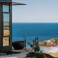 The accommodation and outdoor bath have sweeping views over the ocean and rolling hills on Kangaroo Island